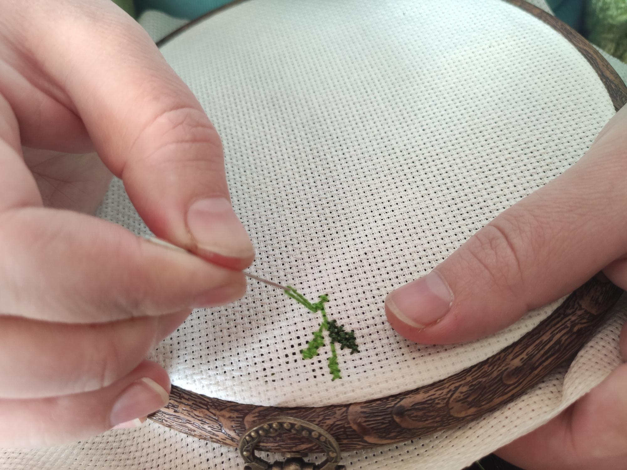 Hands stitching a floral motif on linen